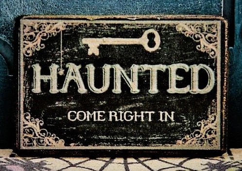 A welcome sign in front of a door and on a spider web welcome mat that says 'Haunted Come Right In'